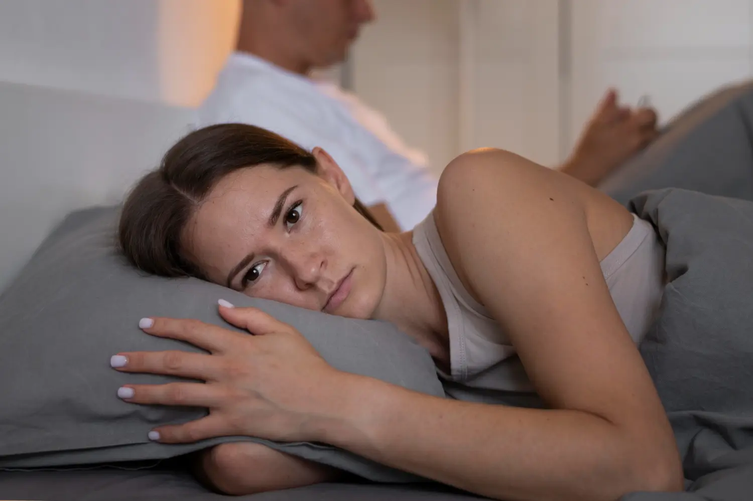 Woman lying awake beside her partner while sexual anxiety creates emotional distance in bed